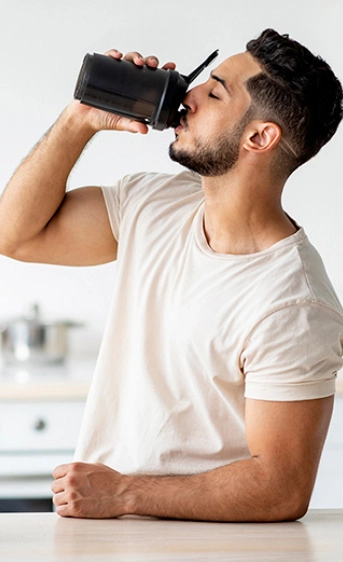 Muškarac u beloj majici pije suplement iz plastične flašice
